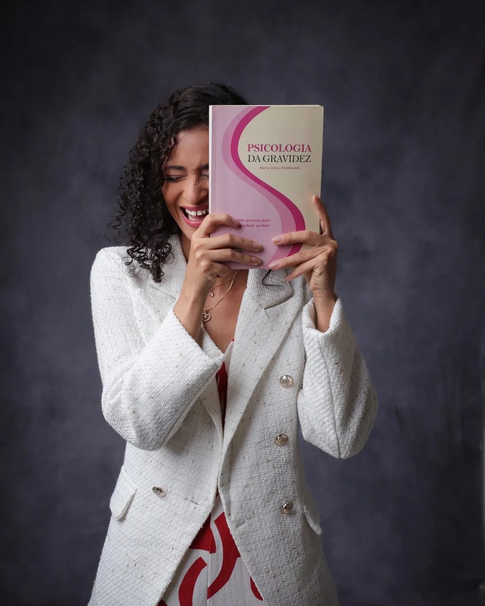 Mayara Sousa rindo enquanto segura o livro Psicologia da Gravidez na frente do rosto